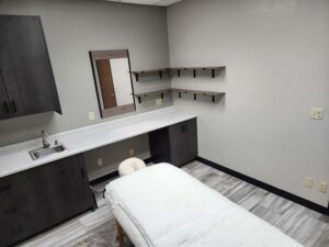 A massage room with a treatment table, cabinets, and The Nail Department and More amenities.