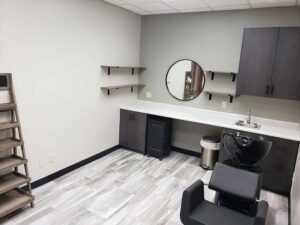 Modern salon room for cosmetologists with styling chair, sink, and nail enhancements counter.