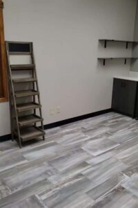Empty room with gray tile floor, wooden shelf ladder, and a cabinet perfect for skincare or nail care.