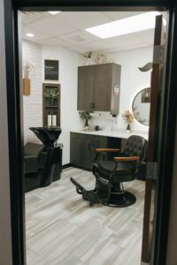 Barber chair and sink in a modern barbershop room with wood cabinets and skincare decor.
