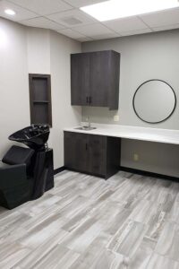 Modern salon room with black shampoo chair, gray cabinets, and natural nail care station.