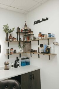 Wall shelves with hair products and decor, plus blue jars for cosmetologists’ natural nail care.