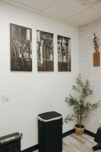 A wall with barber tool art, a trash bin, and a potted plant at The Nail Department and More.