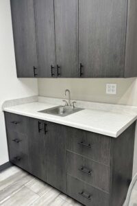Gray cabinets and drawers with a sink, ideal for cosmetologists and natural nail care services.