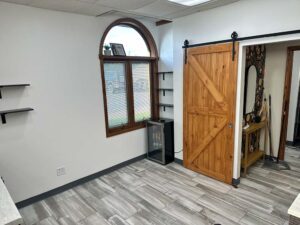 Room with wood barn door, arched window, mini fridge—perfect for Nail Enhancements and More.