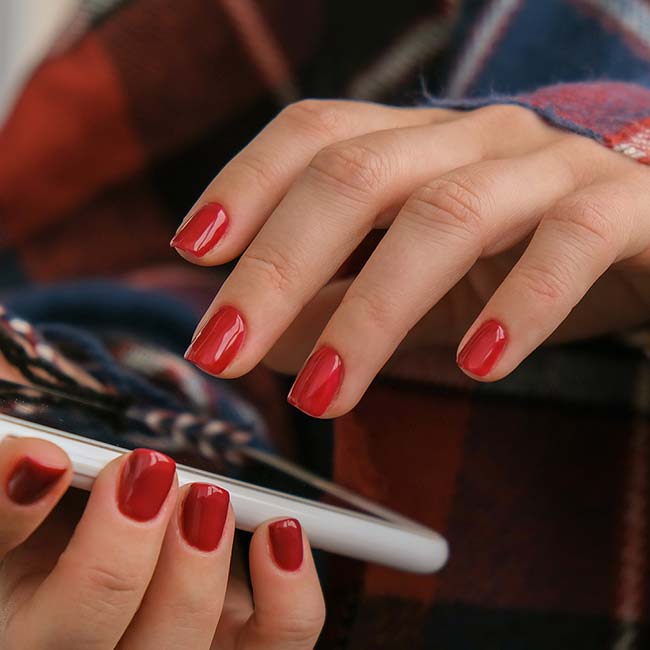 A person with red nail polish, skilled in Natural Nail Care, uses a smartphone in plaid attire.