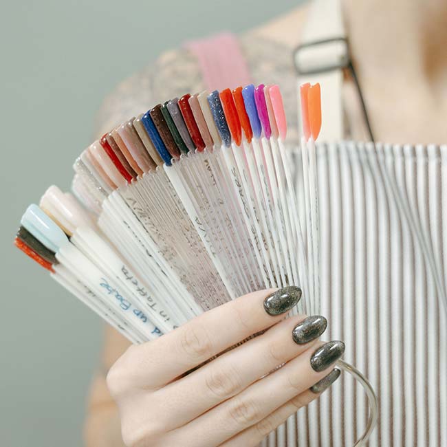 Hand holding nail polish samples, person in striped apron at The Nail Department and More.