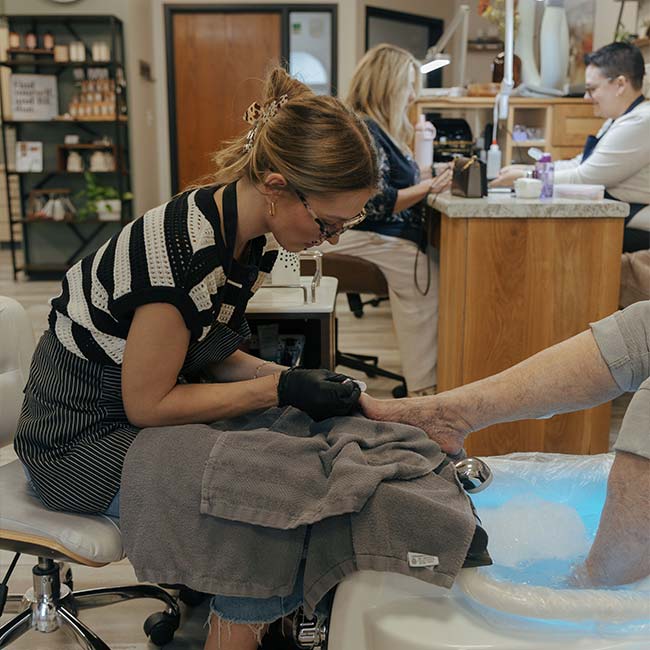 A cosmetologist gives a pedicure to a customer in The Nail Department and More salon.