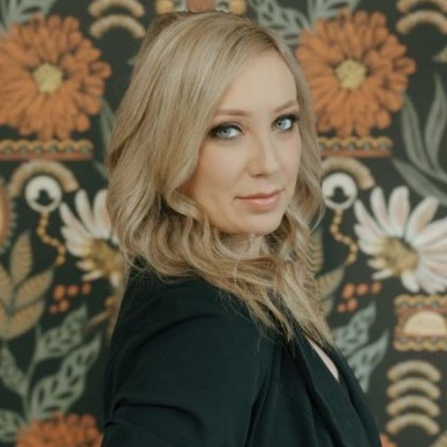 A woman with blonde hair poses as cosmetologists celebrate skincare amid floral patterns.