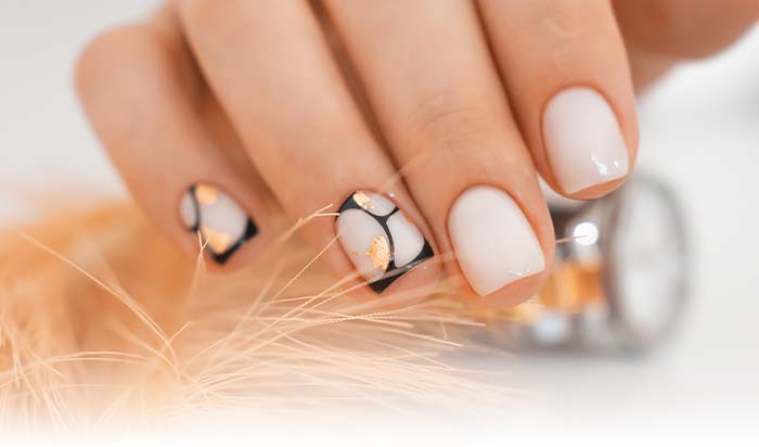 Hand with white and black abstract nail art, holding a polish bottle, showcases Natural Nail Care.