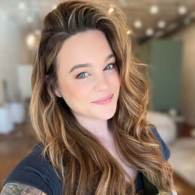 Smiling woman with long wavy hair in a softly lit indoor setting at The Nail Department and More.