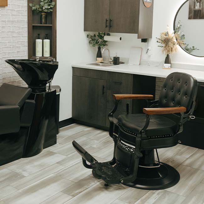 Empty black barber chair and wash station in a salon offering skincare and natural nail care.