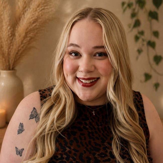 Smiling woman with long blonde hair, butterfly tattoos, and leopard print top at Beauty Professionals Onalaska.
